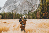 woman with baby in a field looking at trees and mountains